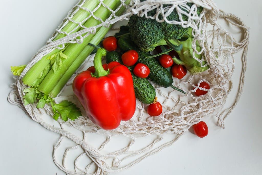 Bright assortment of fresh vegetables including red bell pepper, broccoli, and cherry tomatoes in a mesh bag.